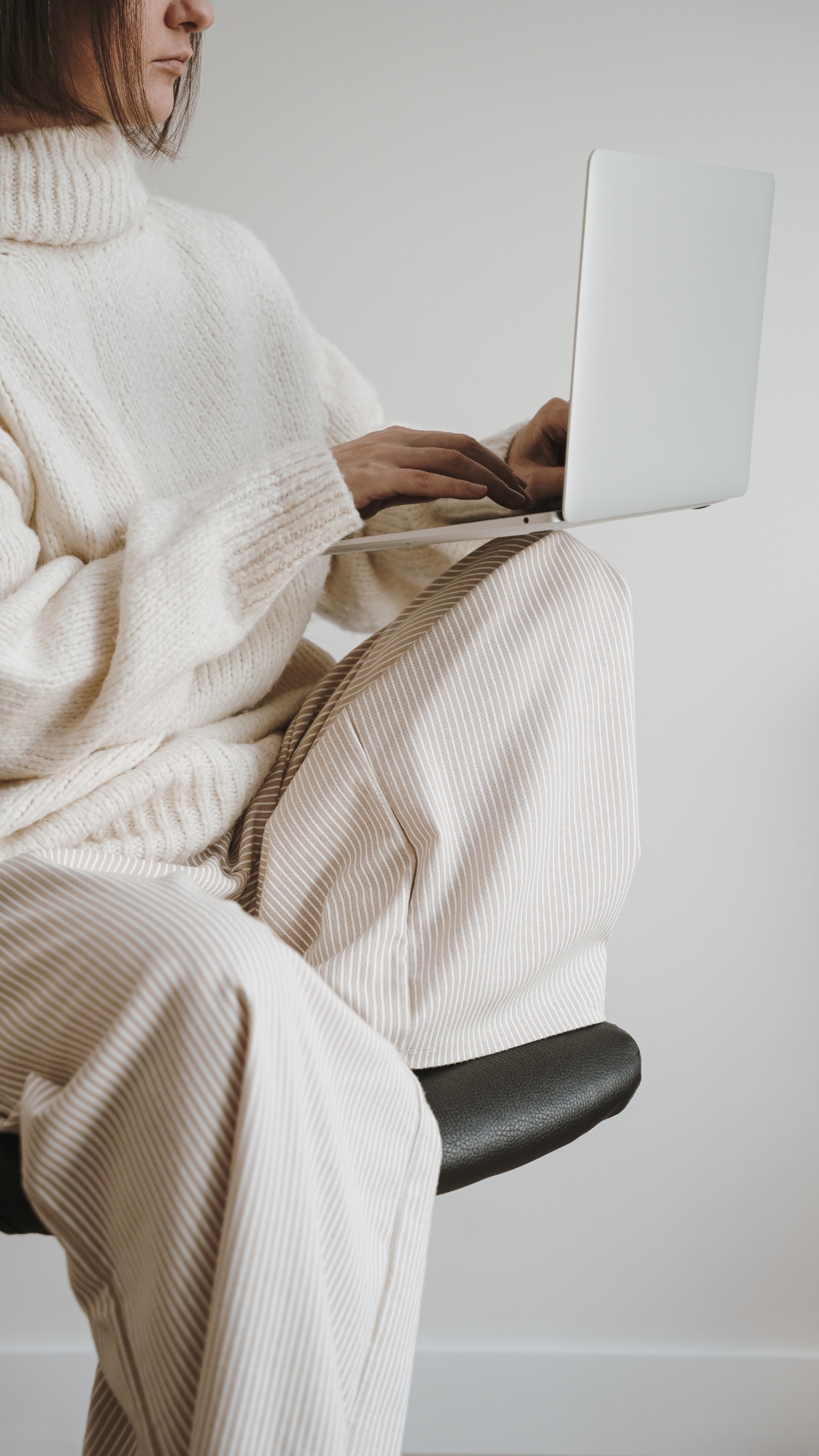 Mujer con ropa clara usando una laptop en un espacio minimalista.